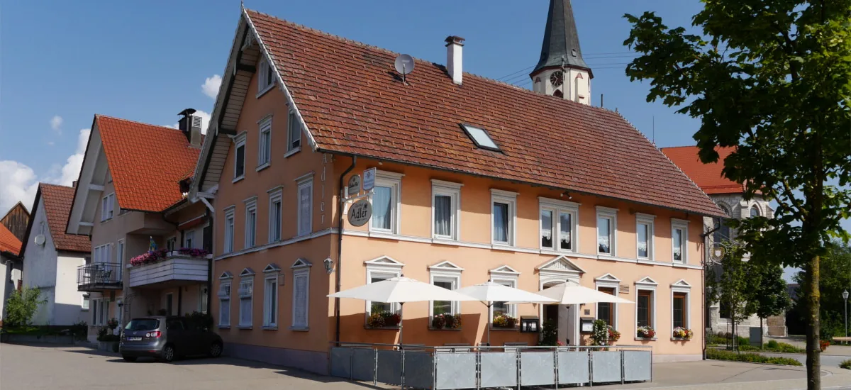 Der Gasthof Adler in Inneringen mit Sonnenschirmen auf der Terrasse und der Kirche im Hintergrund
